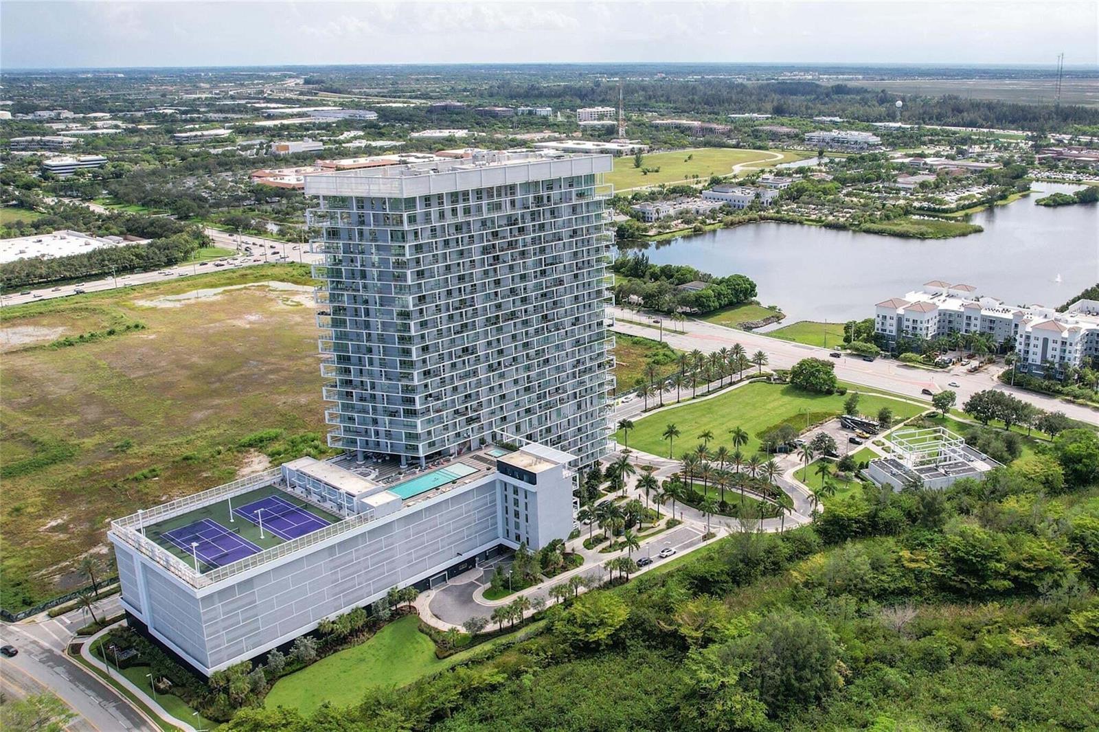 An aerial view of a modern high-rise apartment building with a rooftop tennis court — 2000 Metropica Way # 1509, Sunrise FL 33323, SUNRISE, FL