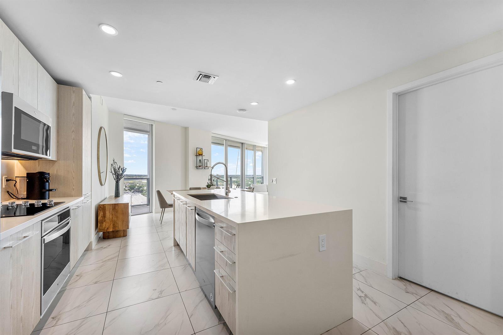 A modern kitchen features light wood cabinetry, a quartz island, and white marble-look tile flooring — 2000 Metropica Way # 1509, Sunrise FL 33323, SUNRISE, FL