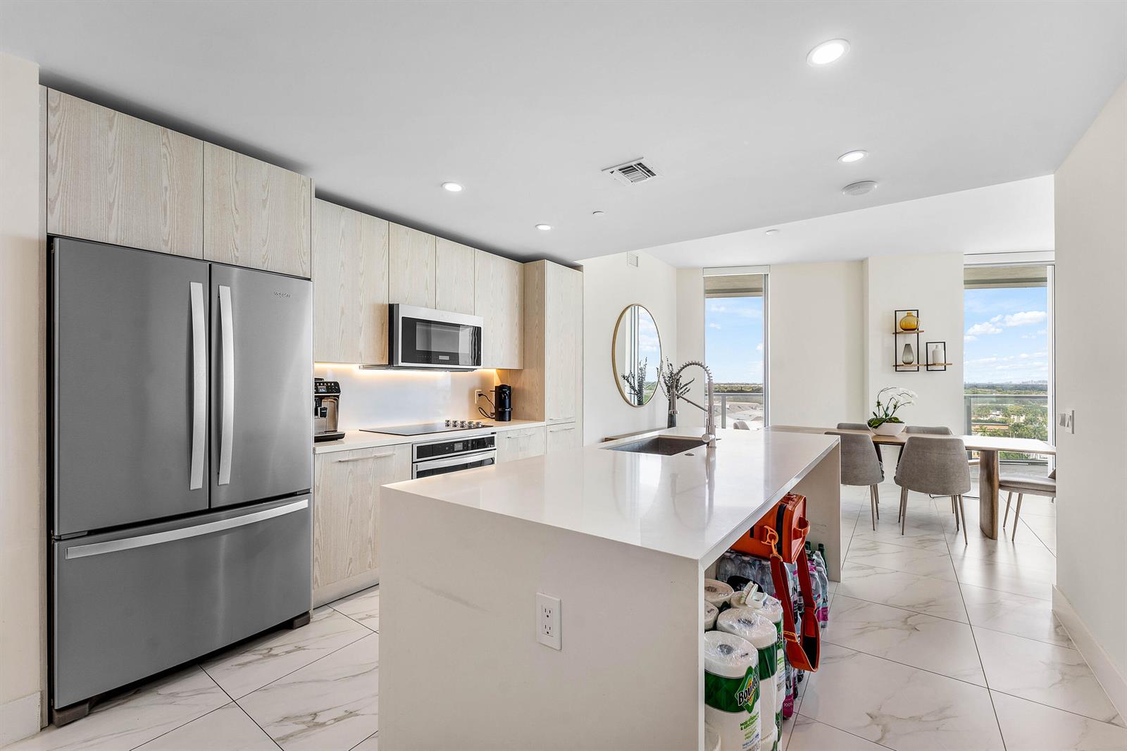 A modern kitchen features light wood cabinetry, a white quartz island, and stainless steel appliances — 2000 Metropica Way # 1509, Sunrise FL 33323, SUNRISE, FL