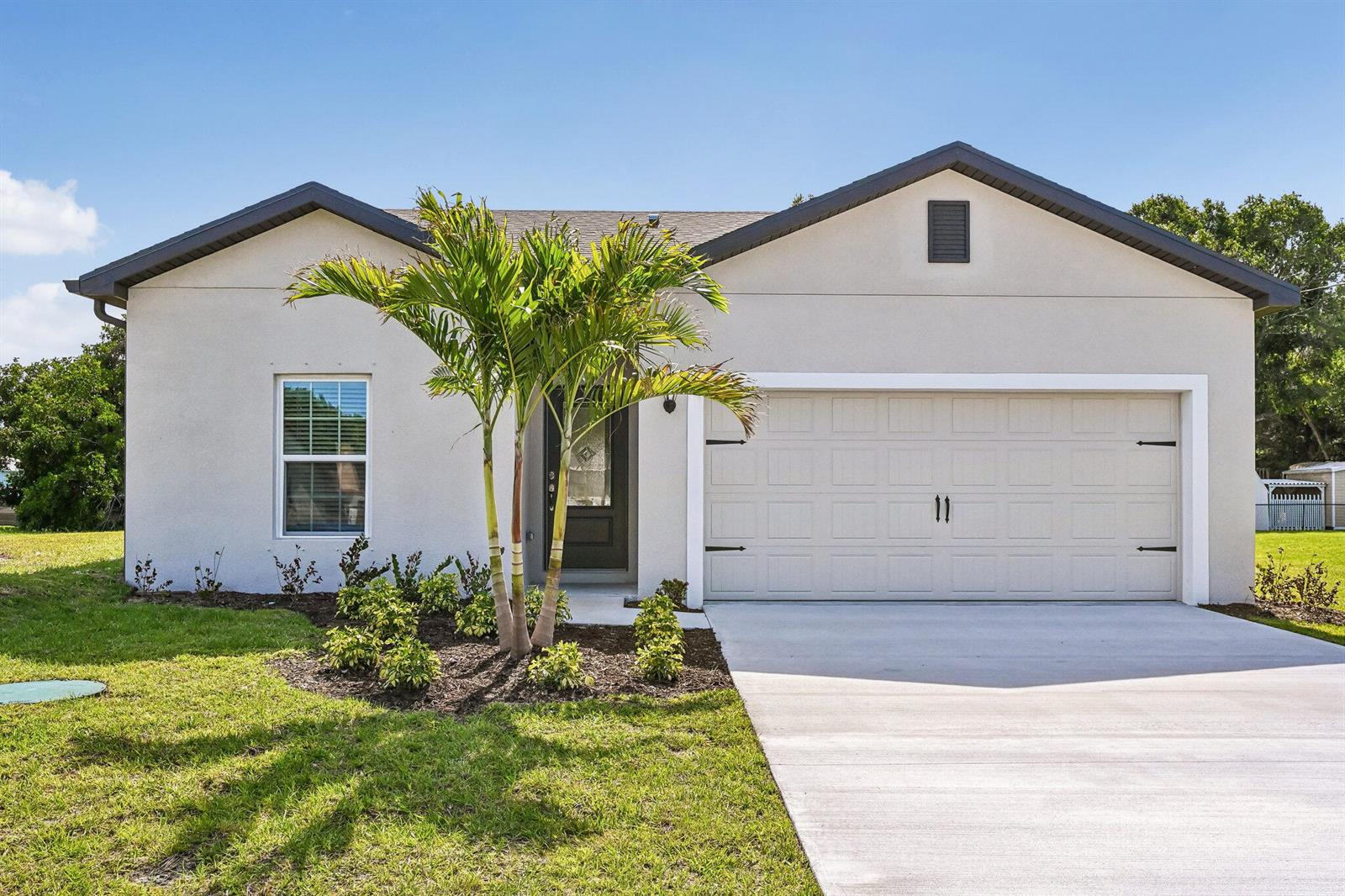A single-story house features a light-colored stucco exterior, a two-car garage, and a palm tree — 5200 Hickory Drive, Fort Pierce FL 34982, FORT PIERCE, FL