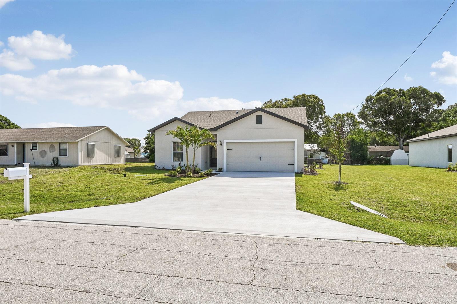 A single-story house with a concrete driveway and a two-car garage under a blue sky — 5200 Hickory Drive, Fort Pierce FL 34982, FORT PIERCE, FL