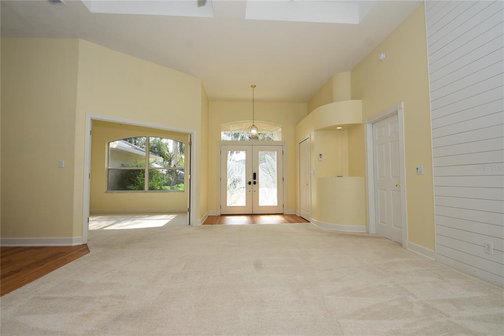 A spacious living room features beige carpeting, yellow walls, a white shiplap wall, and double-door entry — 1216 HAMPSTEAD LANE, ORMOND BEACH, FL
