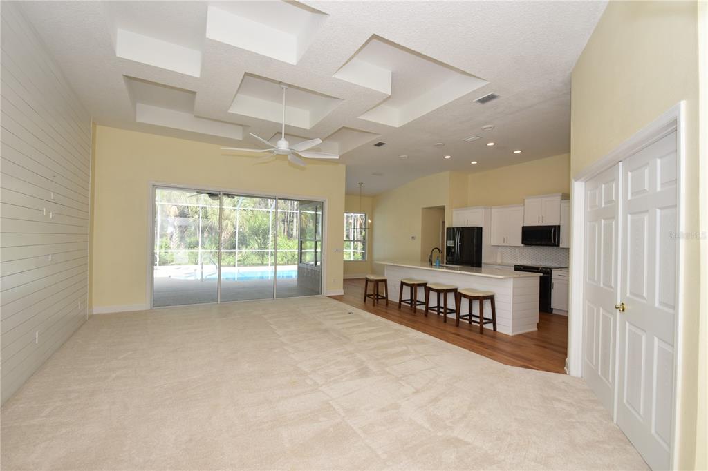An open-concept living area with a coffered ceiling, carpeted flooring, and a kitchen with island — 1216 HAMPSTEAD LANE, ORMOND BEACH, FL