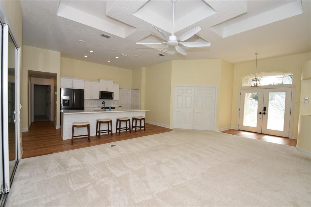 An open-concept living area features a kitchen with an island, white cabinetry, and carpeted flooring — 1216 HAMPSTEAD LANE, ORMOND BEACH, FL