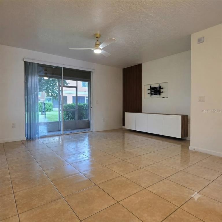 A living room with beige tile flooring, a ceiling fan, and a sliding glass door — 1561 CHELSEA DRIVE, DAVENPORT, FL