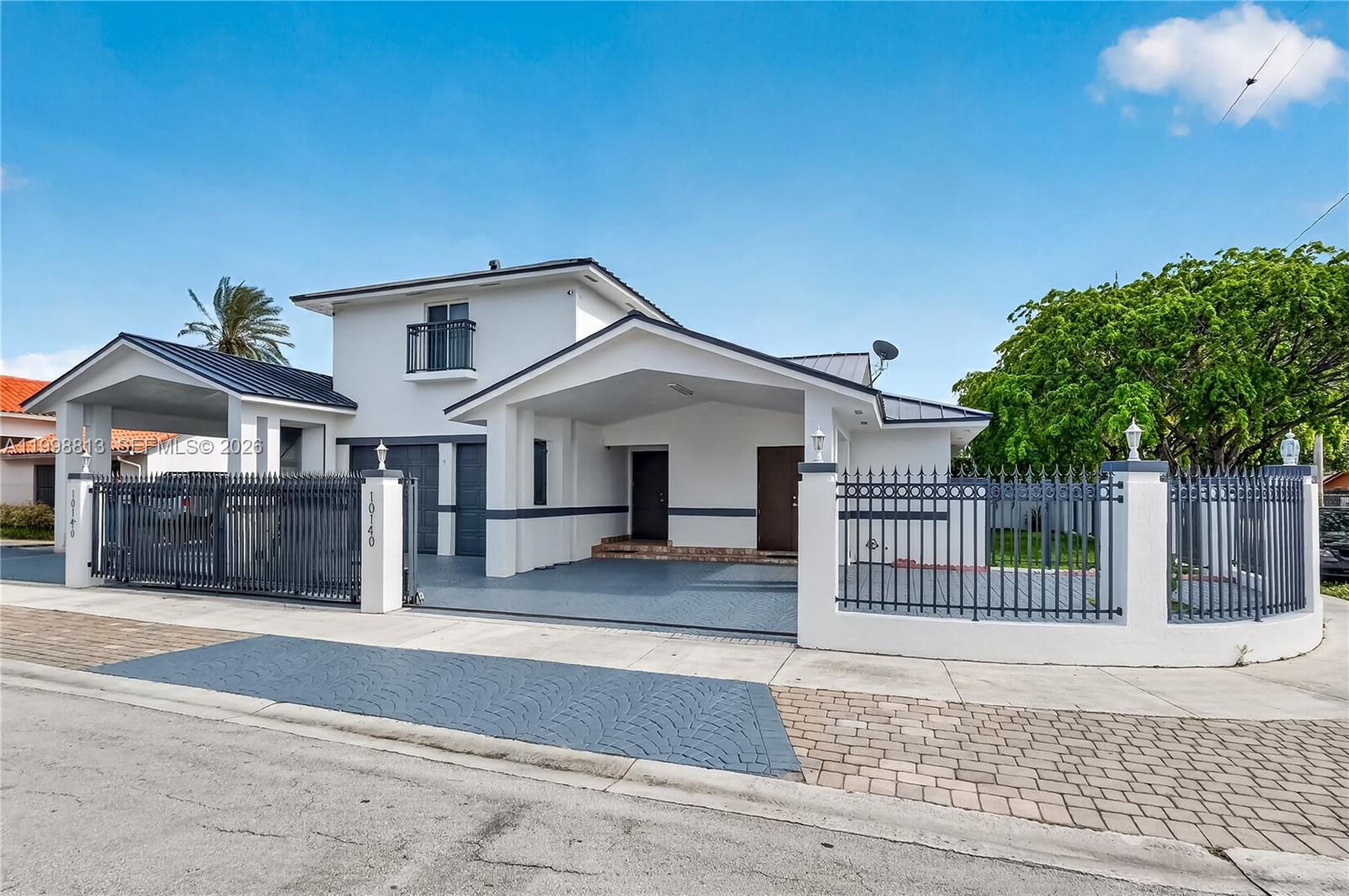A white two-story house features a gated driveway, a covered carport, and a metal roof — 10140 SW 26th Ter, Miami FL 33165, MIAMI, FL