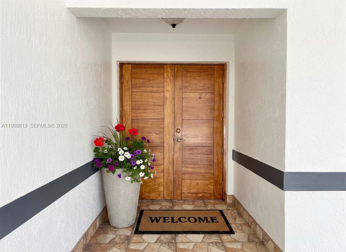 A wooden double door entrance features a potted plant and a welcome mat — 10140 SW 26th Ter, Miami FL 33165, MIAMI, FL