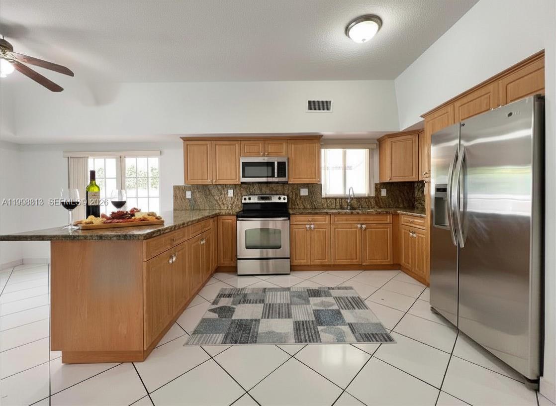 A kitchen features light wood cabinets, granite countertops, stainless steel appliances, and white tile flooring — 10140 SW 26th Ter, Miami FL 33165, MIAMI, FL