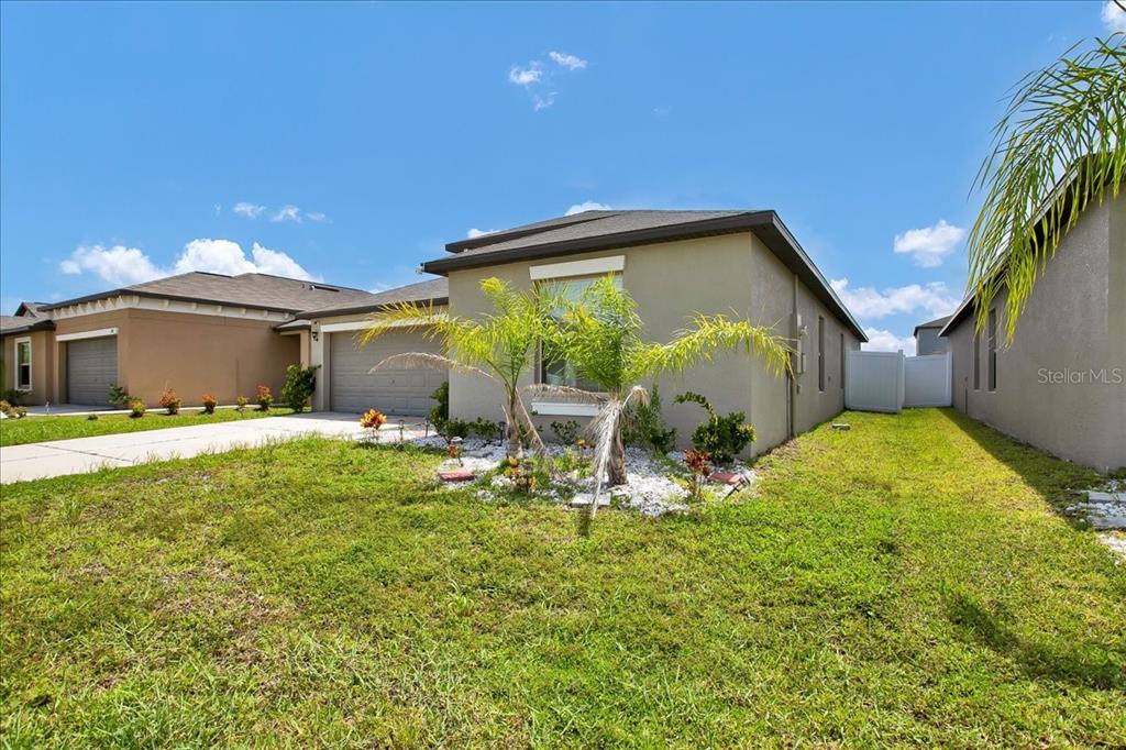 A single-story house exterior with a tan stucco facade, a two-car garage, and palm trees — 769 CALICO SCALLOP STREET, RUSKIN, FL