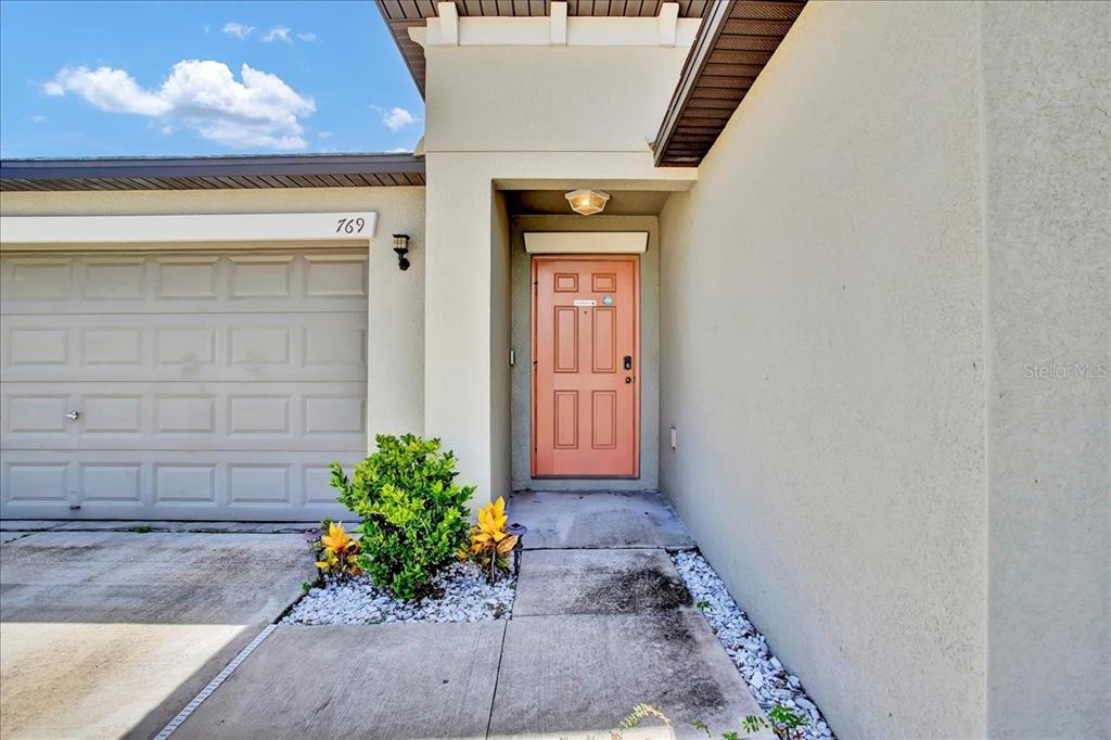 A tan house exterior features a beige garage door, a coral front door, and landscaping — 769 CALICO SCALLOP STREET, RUSKIN, FL