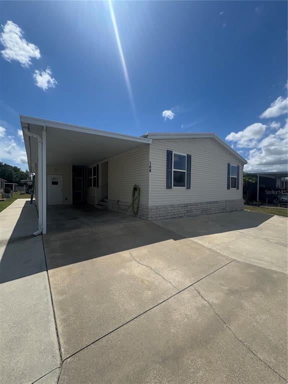 A light-colored mobile home with a carport and concrete driveway under a blue sky — 106 REINEKE ROAD, HAINES CITY, FL