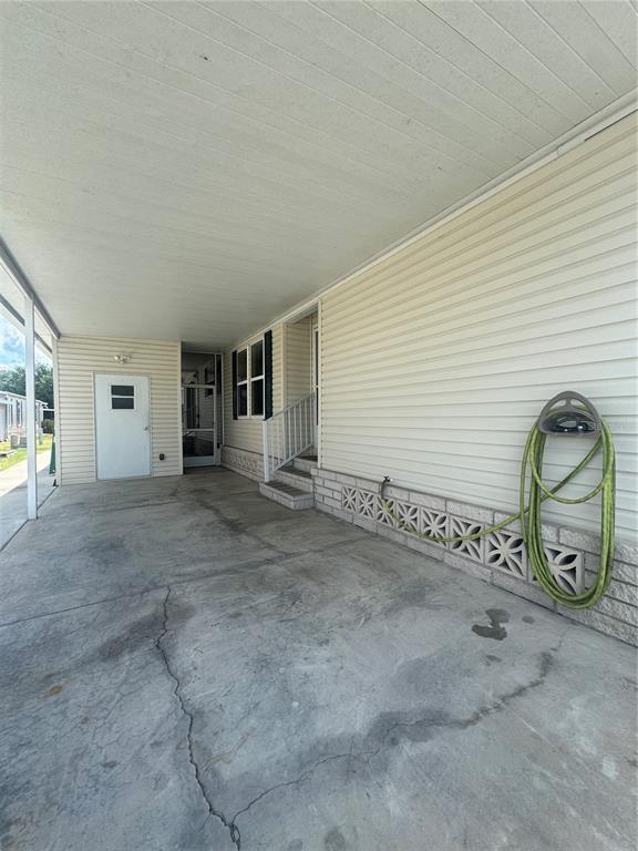 A concrete carport features a white door, a garden hose, and decorative concrete blocks — 106 REINEKE ROAD, HAINES CITY, FL