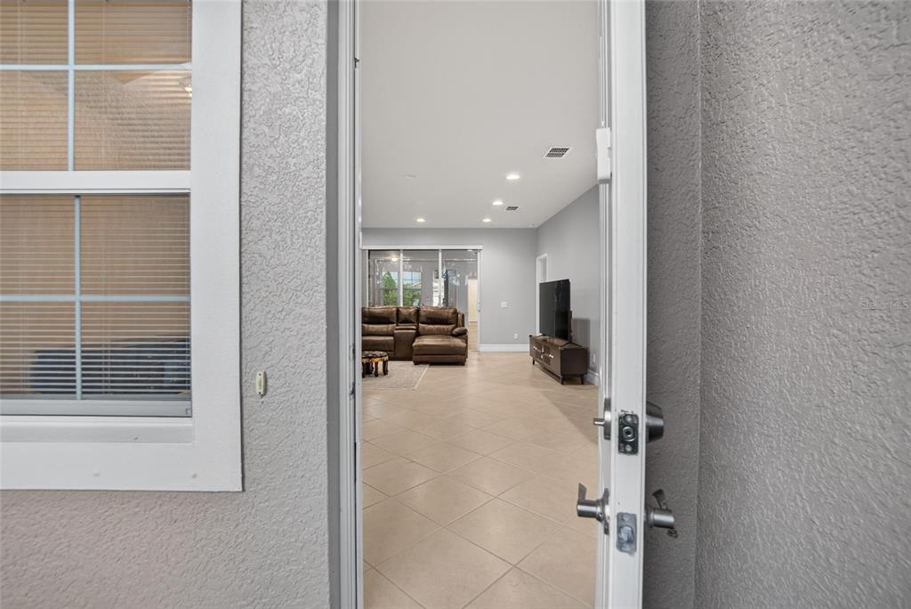 A view from an open doorway into a living room with tile floors and furniture — 16216 AMETHYST KEY DRIVE, WIMAUMA, FL