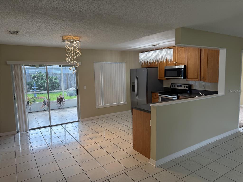 A kitchen and dining area with tile floors, wooden cabinets, and two crystal chandeliers — 1069 BRIDLEWOOD WAY, BRANDON, FL