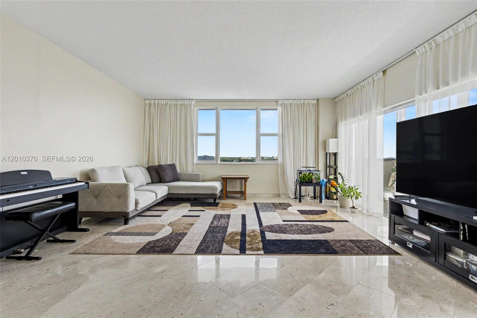 A living room features a sectional sofa, a piano, a large area rug, and floor-to-ceiling windows — 3800 Hillcrest Dr # 1211, Hollywood FL 33021, HOLLYWOOD, FL