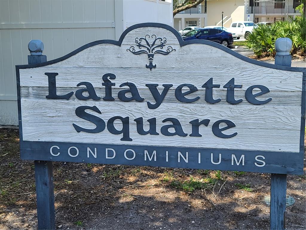 A wooden sign for Lafayette Square Condominiums stands outdoors in front of a parking area — 101 LAKE AVENUE NE UNIT 222, LARGO, FL