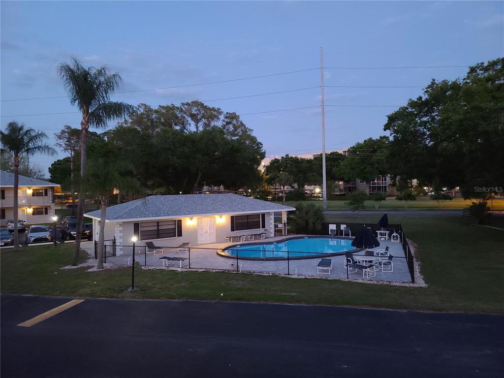 An outdoor swimming pool and a small building are surrounded by a black metal fence — 101 LAKE AVENUE NE UNIT 222, LARGO, FL