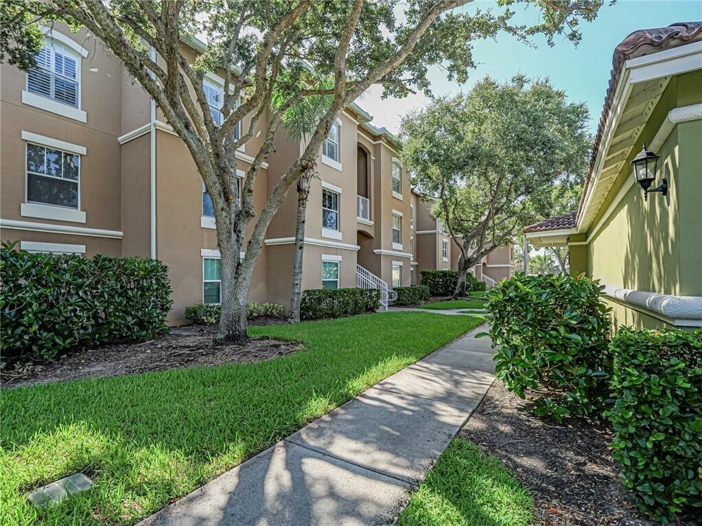 A sidewalk leads past a multi-story apartment building with tan stucco walls and green landscaping — 5095 Fairways Circle # I303, Vero Beach FL 32967, VERO BEACH, FL