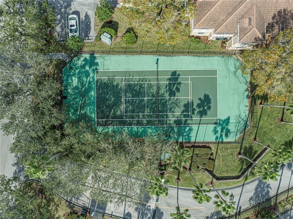 An aerial view shows a fenced tennis court surrounded by trees, landscaping, and a nearby building — 5095 Fairways Circle # I303, Vero Beach FL 32967, VERO BEACH, FL