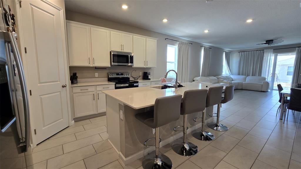 A kitchen with white cabinets, a central island with bar stools, and an open living area — 802 BALLANTYNE DRIVE, LAKE WALES, FL