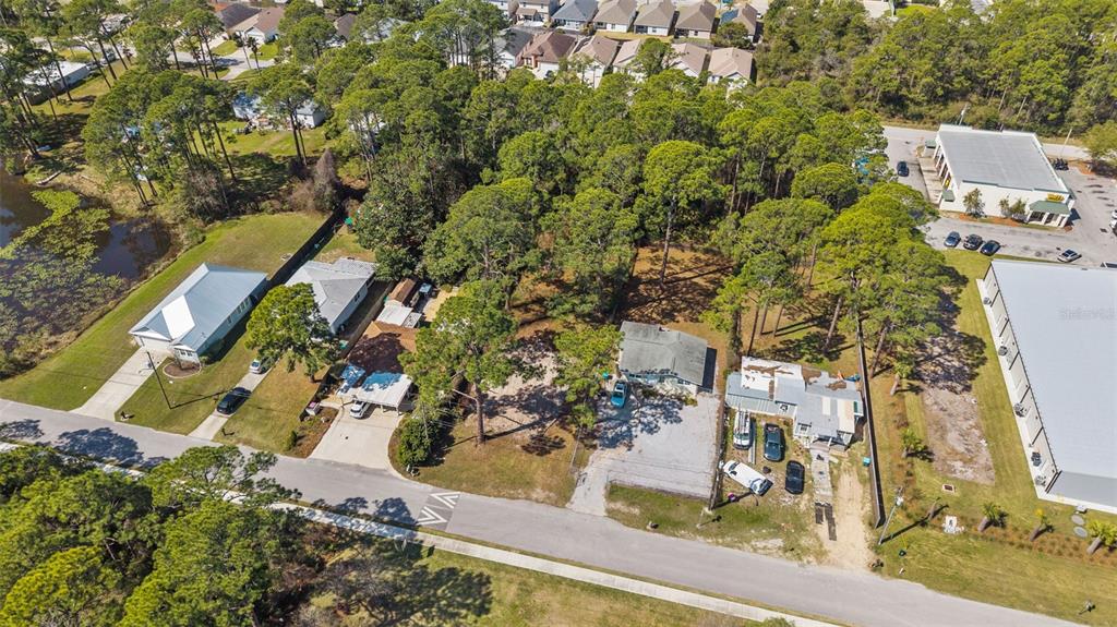An aerial view shows several houses and commercial buildings surrounded by trees and a pond — 112 BETH STREET, PANAMA CITY BEACH, FL