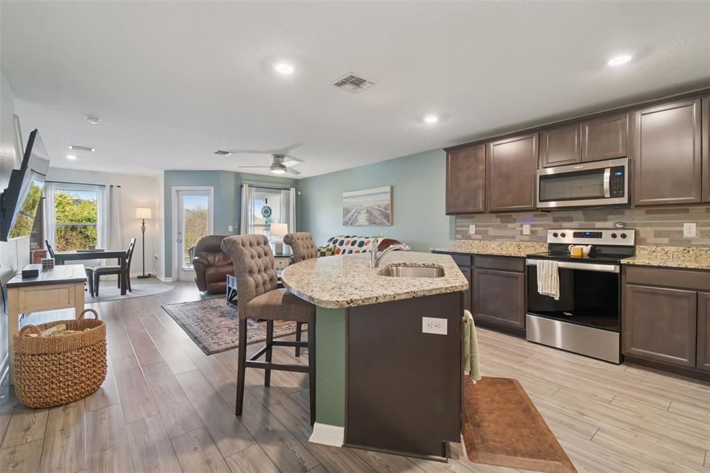An open-concept kitchen and living area features dark wood cabinets, granite countertops, and wood-look flooring — 5228 NEW FRIENDSHIP PLACE, TAMPA, FL