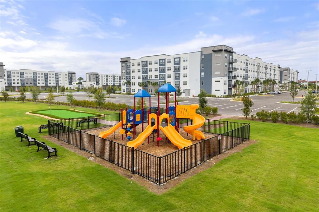 A fenced playground with slides sits on a grassy lawn in front of apartment buildings — 5587 MILLENIA PARK BOULEVARD UNIT 308, ORLANDO, FL