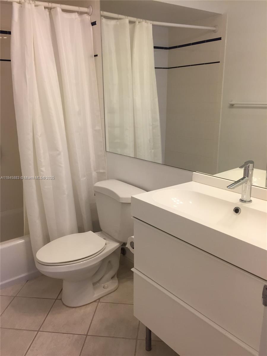 A bathroom features a white vanity, a toilet, and a shower with a white curtain — 201 Sunrise Drive # 102, Key Biscayne FL 33149, KEY BISCAYNE, FL