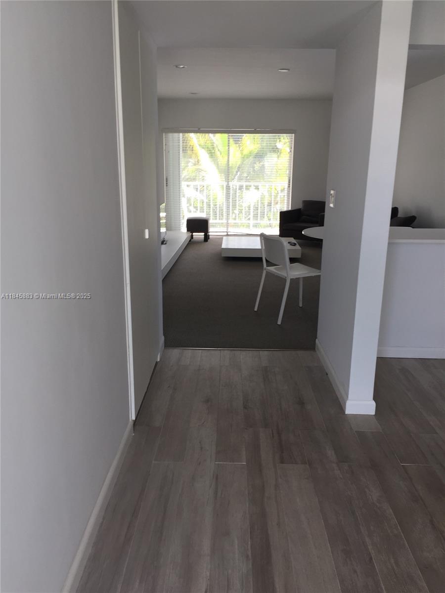 A view from a hallway with wood-look flooring into a carpeted living area with balcony — 201 Sunrise Drive # 102, Key Biscayne FL 33149, KEY BISCAYNE, FL