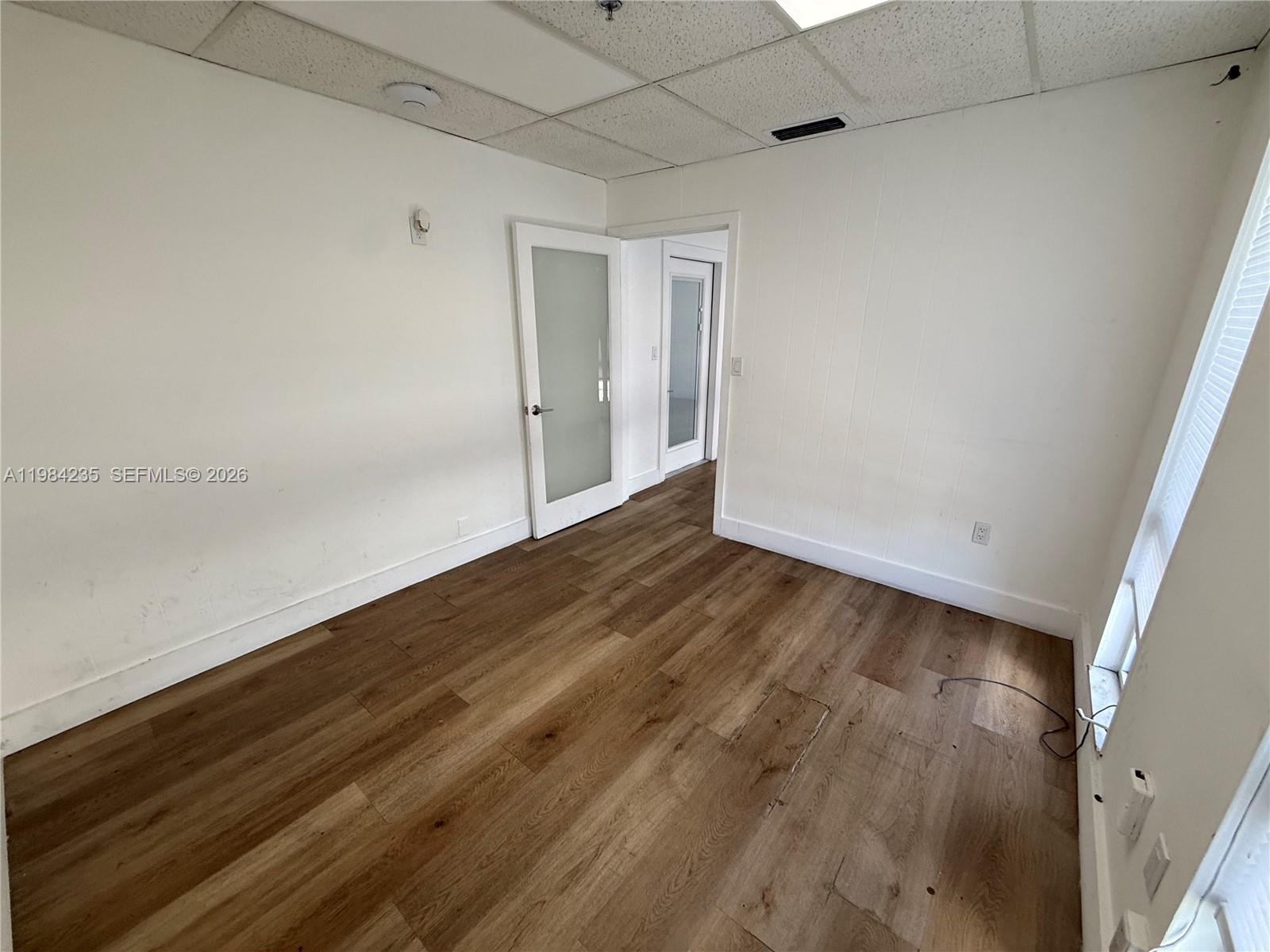 An empty room features wood-look flooring, white walls, a drop ceiling, and two glass-paneled doors — 810 NE 125th St, North Miami FL 33161, NORTH MIAMI, FL