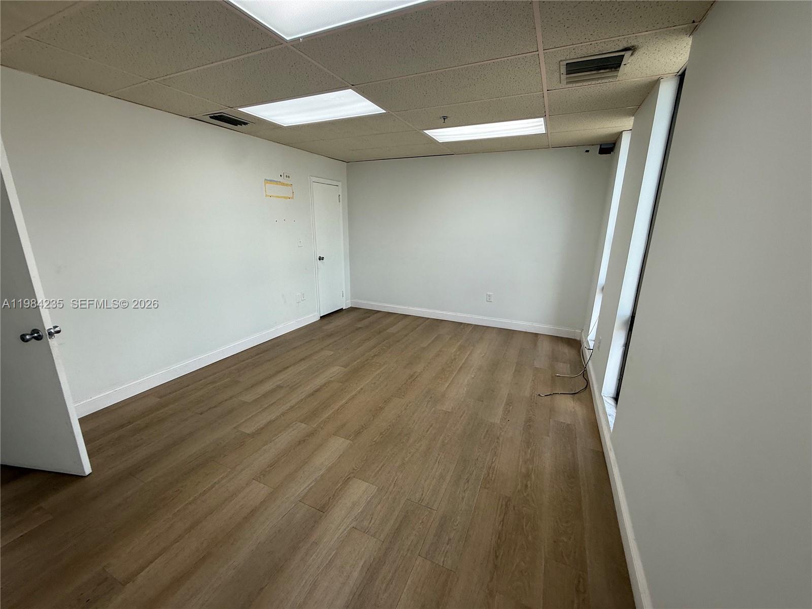 An empty office space features white walls, wood-look flooring, and a drop ceiling — 810 NE 125th St, North Miami FL 33161, NORTH MIAMI, FL