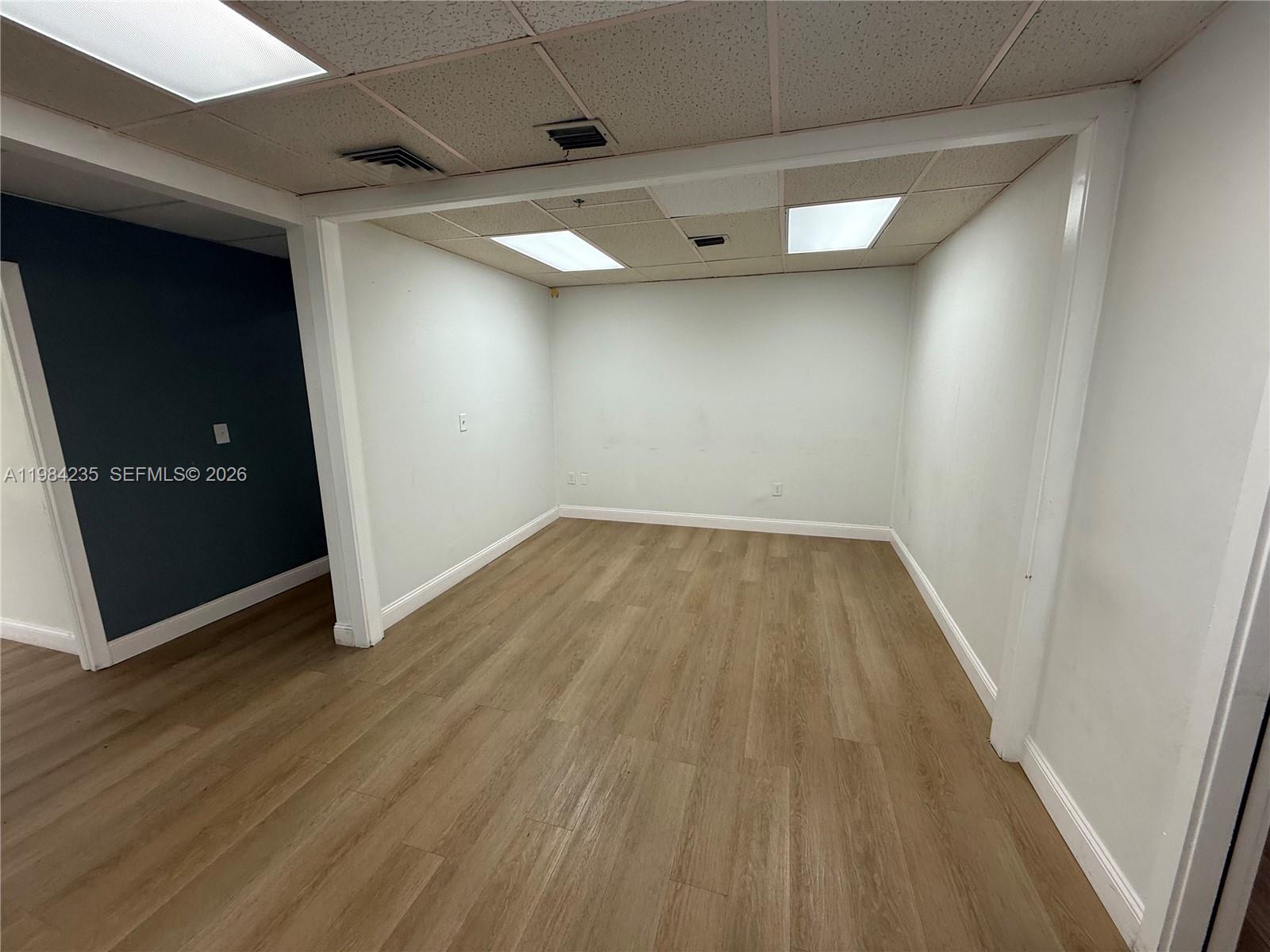 An empty office space features light wood-look flooring, white walls, and a drop ceiling — 810 NE 125th St, North Miami FL 33161, NORTH MIAMI, FL