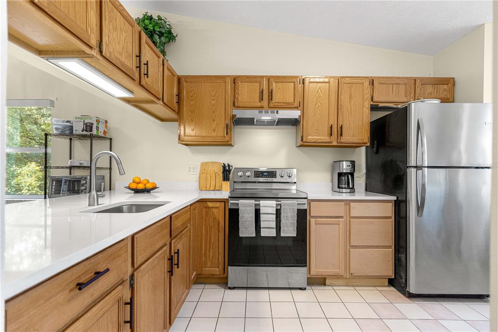 A kitchen features oak cabinets, white countertops, stainless steel appliances, and a tiled floor — 10457 SW 85TH COURT, OCALA, FL