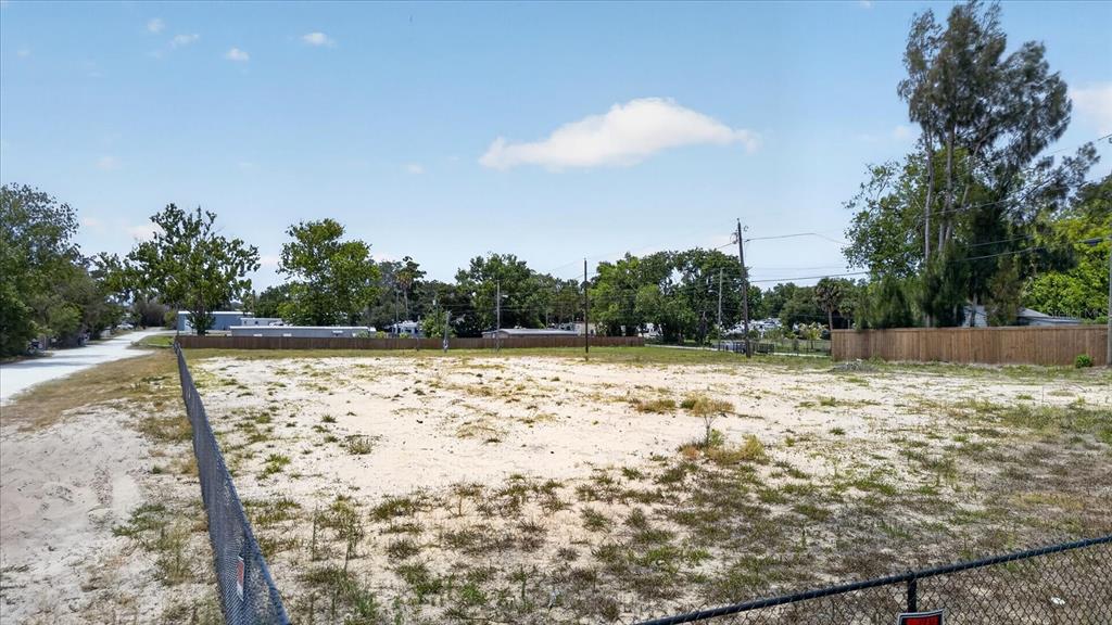 A vacant, sandy lot is enclosed by a chain-link fence under a blue sky — 4710 TROUBLE CREEK ROAD, NEW PORT RICHEY, FL