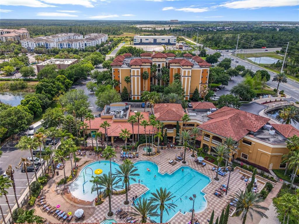 An aerial view shows a large resort-style swimming pool with palm trees and surrounding buildings — 12539 FLORIDAYS RESORT DRIVE UNIT 112D, ORLANDO, FL