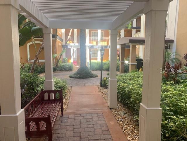 A covered walkway with a wooden bench leads to a landscaped courtyard between apartment buildings — 12539 FLORIDAYS RESORT DRIVE UNIT 112D, ORLANDO, FL