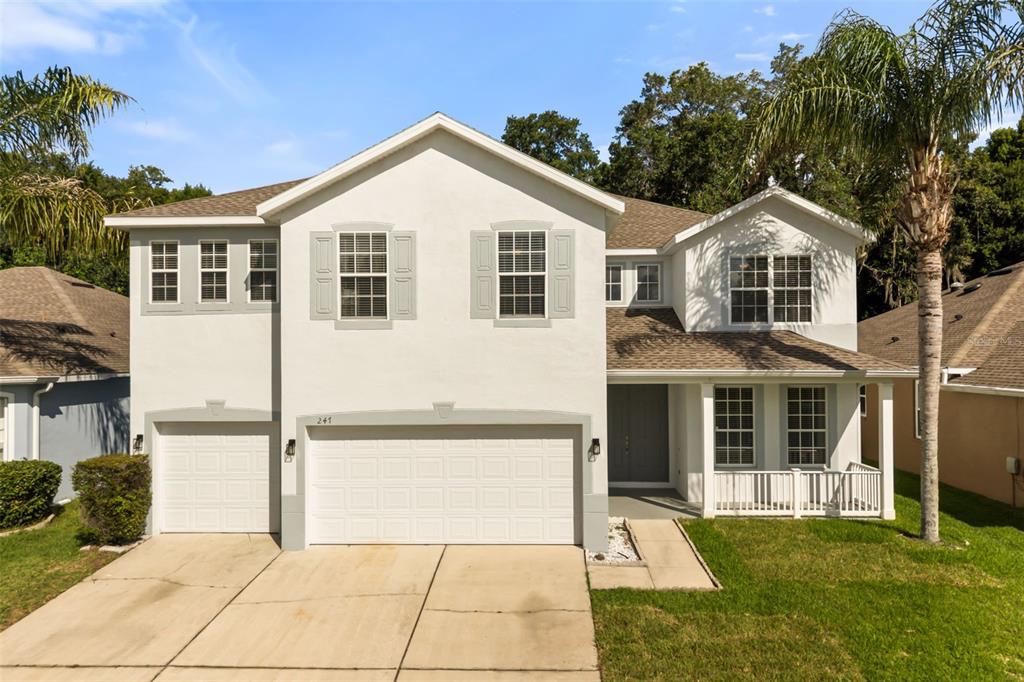 A two-story suburban house with a three-car garage, light stucco exterior, and a front porch — 247 MAGNOLIA PARK TRAIL, SANFORD, FL