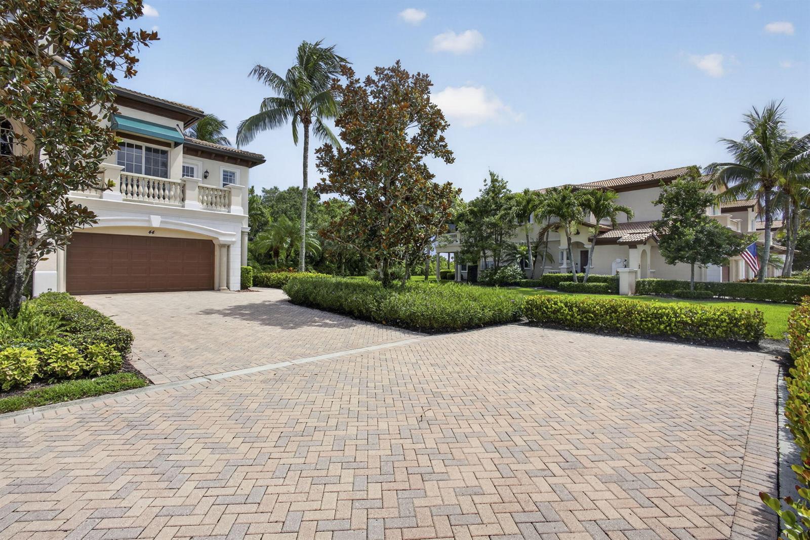 A paved driveway leads to a two-story house with a garage and palm trees — 222 Tresana Boulevard # 44, Jupiter FL 33478, JUPITER, FL