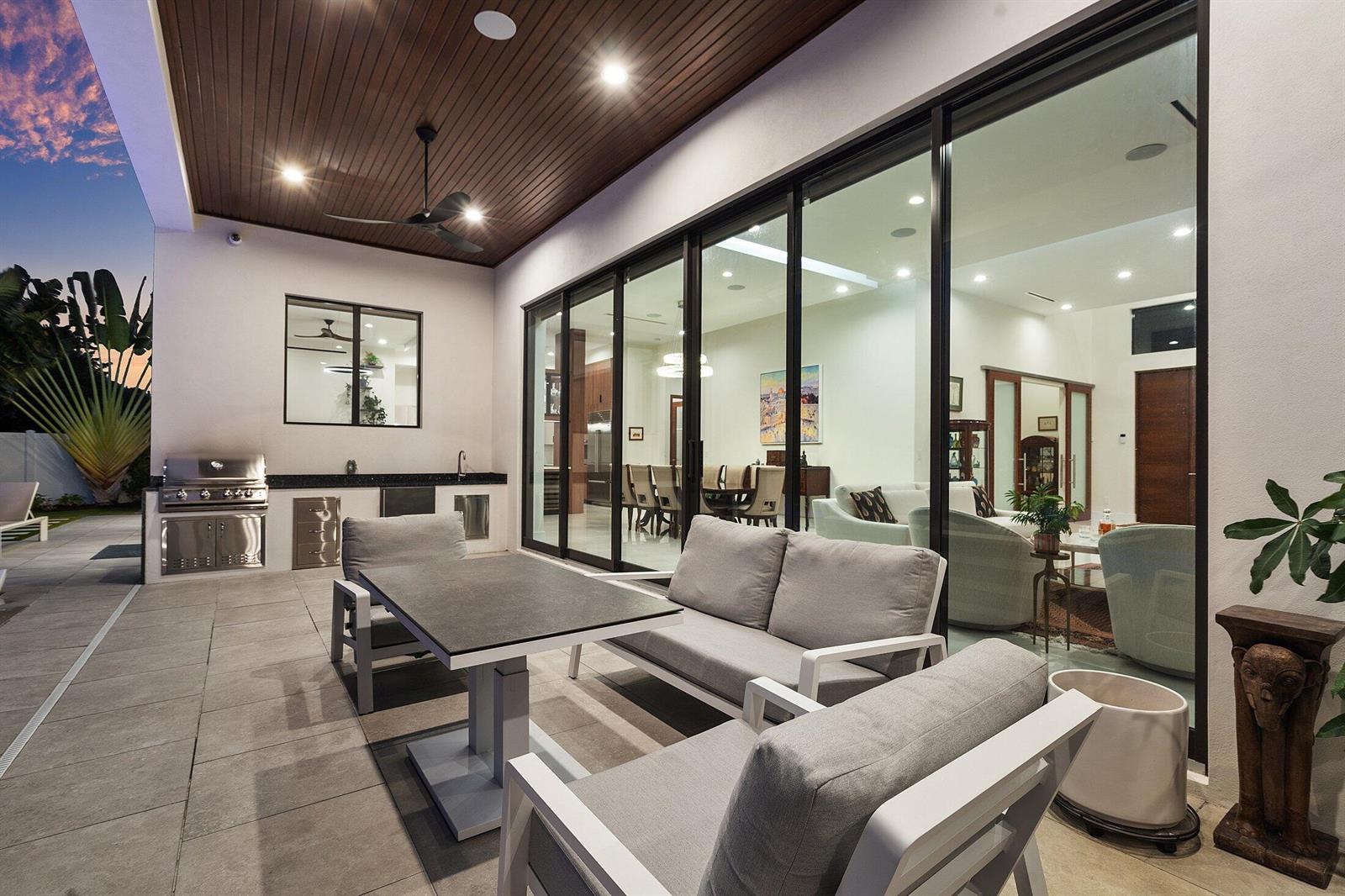 A covered outdoor patio features a dining set, lounge seating, and a built-in stainless grill — 450 NE 10th Street, Boca Raton FL 33432, BOCA RATON, FL