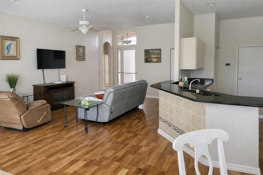 A living room with wood flooring, a grey sofa, and a kitchen breakfast bar — 18146 AVONSDALE CIRCLE, PORT CHARLOTTE, FL