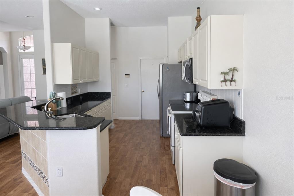 A kitchen features white cabinets, black granite countertops, stainless steel appliances, and wood-look flooring — 18146 AVONSDALE CIRCLE, PORT CHARLOTTE, FL