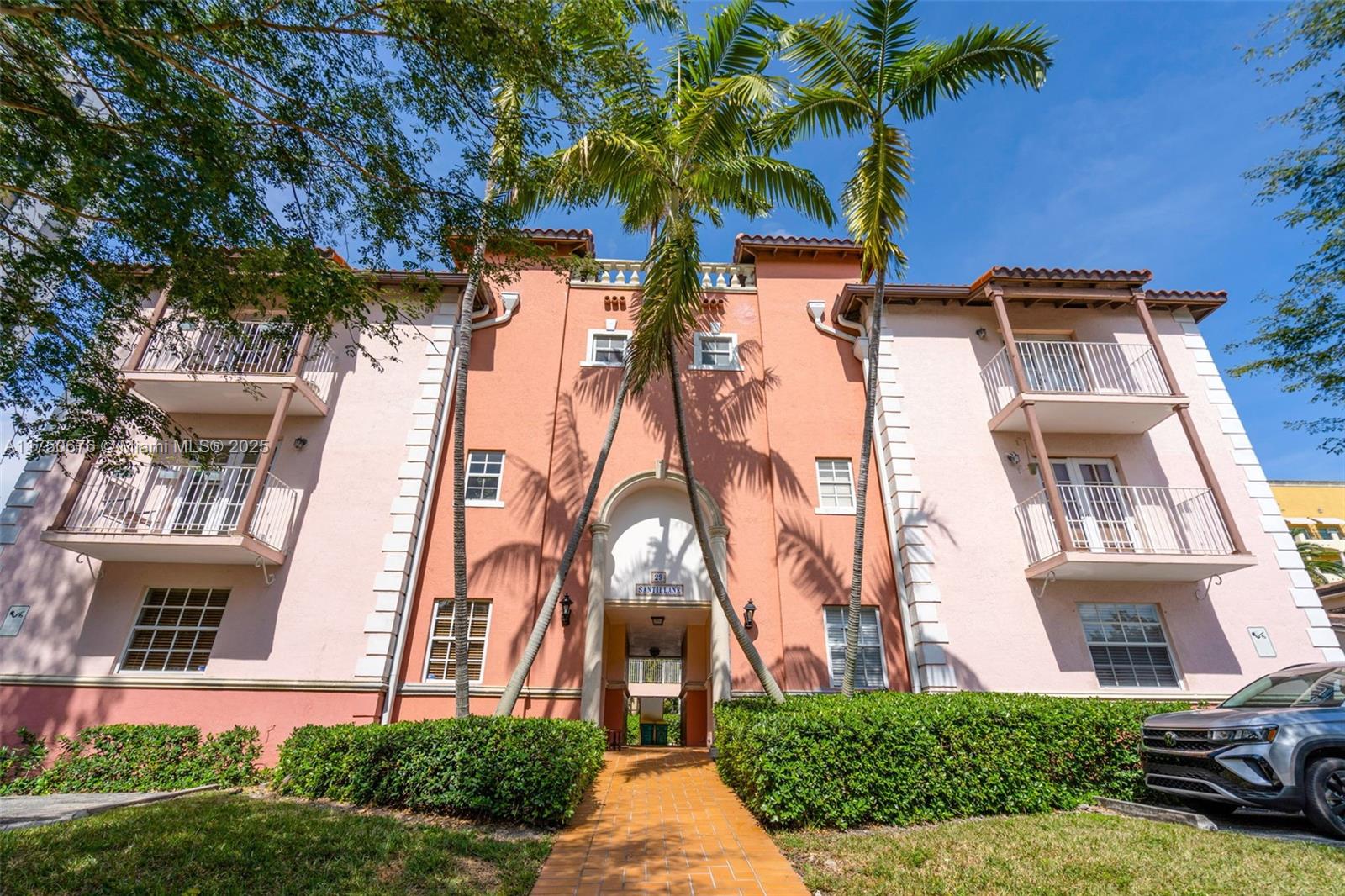 A three-story peach-colored apartment building features balconies, palm trees, and a central arched entrance — 29 Santillane Ave # 7, Coral Gables FL 33134, CORAL GABLES, FL