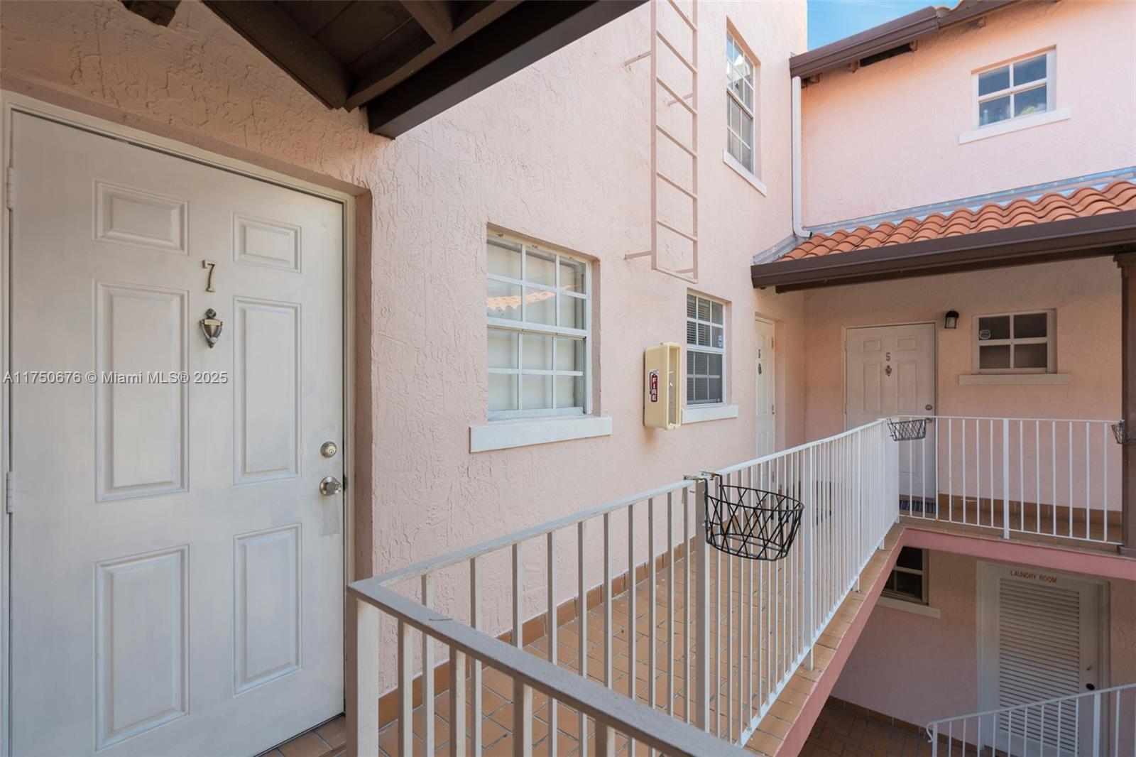 An exterior walkway with a white railing connects apartment doors in a pink stucco building — 29 Santillane Ave # 7, Coral Gables FL 33134, CORAL GABLES, FL