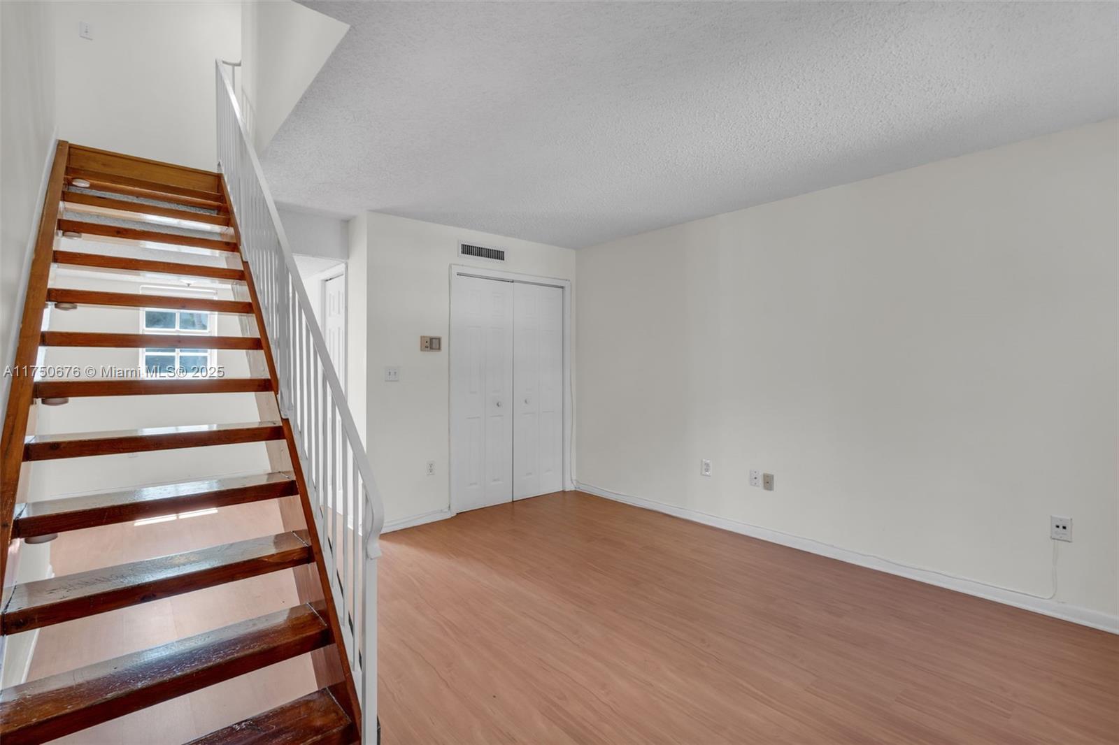 An empty room features wood-look flooring, white walls, a closet, and a wooden staircase — 29 Santillane Ave # 7, Coral Gables FL 33134, CORAL GABLES, FL