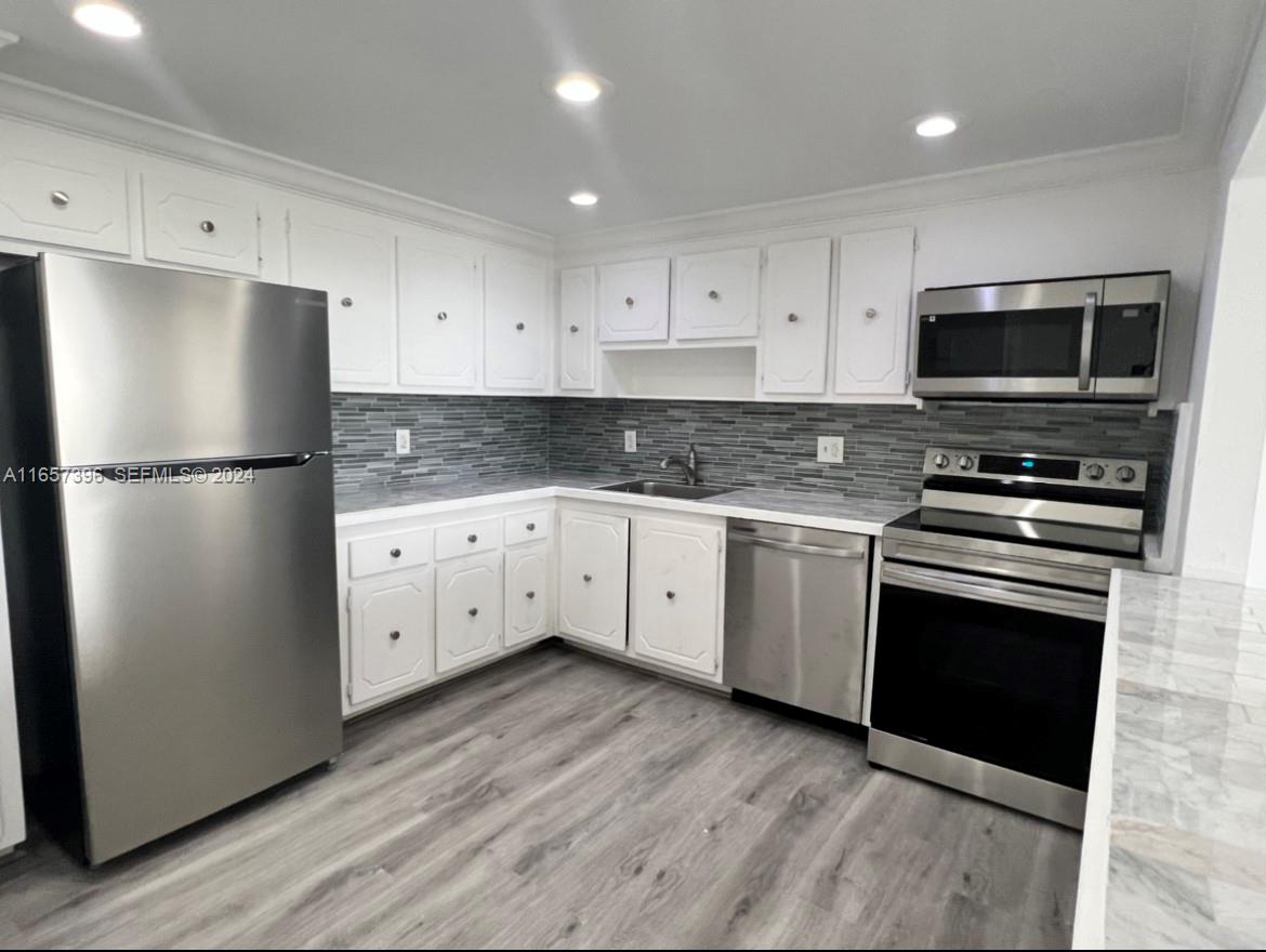 A kitchen features white cabinets, stainless steel appliances, a gray tiled backsplash, and wood-look flooring — 13499 Biscayne Blvd # 1205, North Miami FL 33181, NORTH MIAMI, FL