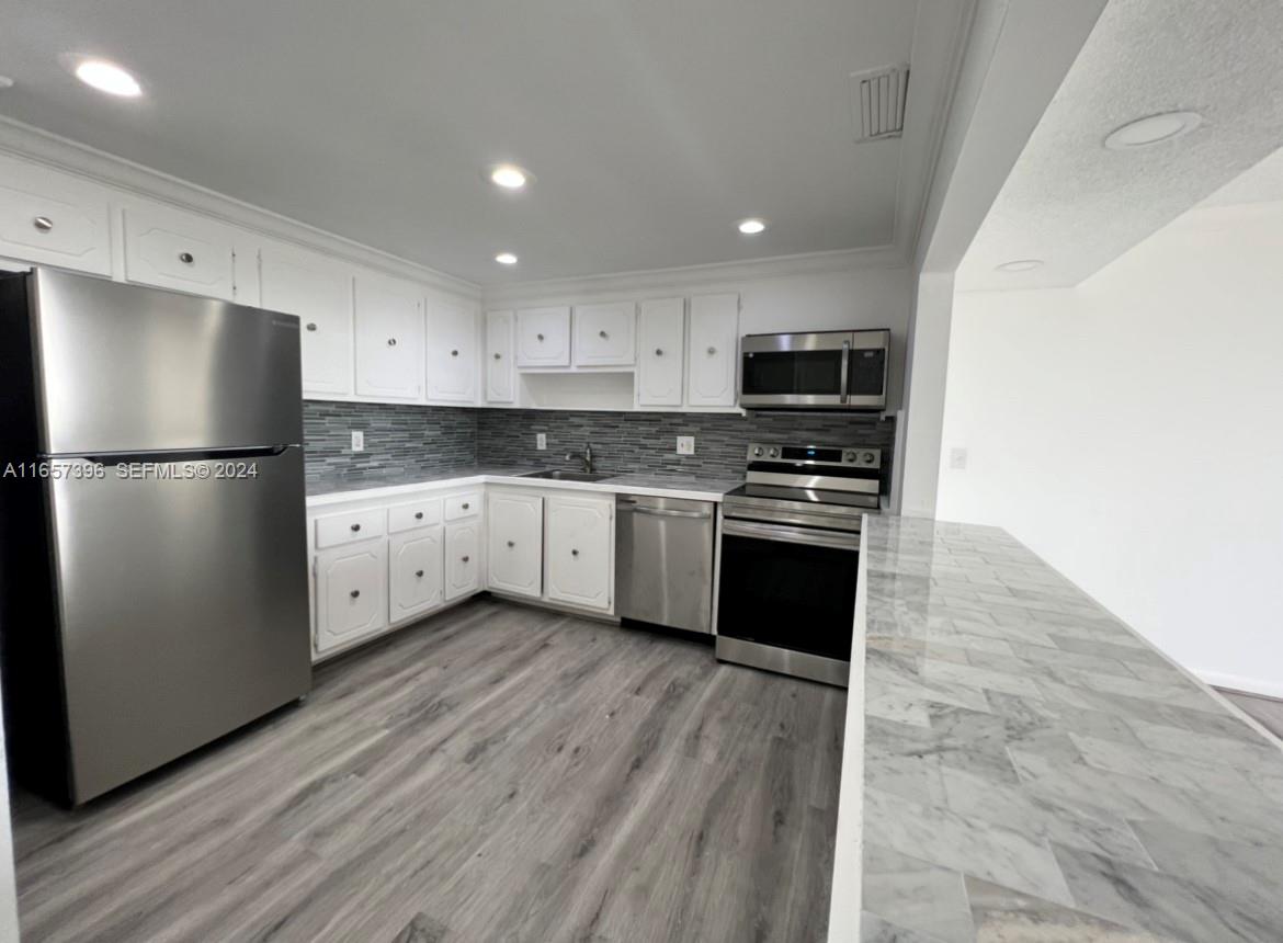 A kitchen features white cabinets, stainless steel appliances, a gray tiled backsplash, and wood-look flooring — 13499 Biscayne Blvd # 1205, North Miami FL 33181, NORTH MIAMI, FL