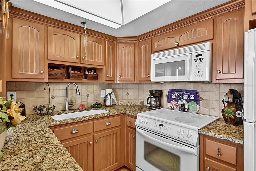 A kitchen features wood cabinets, granite countertops, a white stove, and a microwave — 3013 S ATLANTIC AVENUE UNIT 2060, DAYTONA BEACH, FL