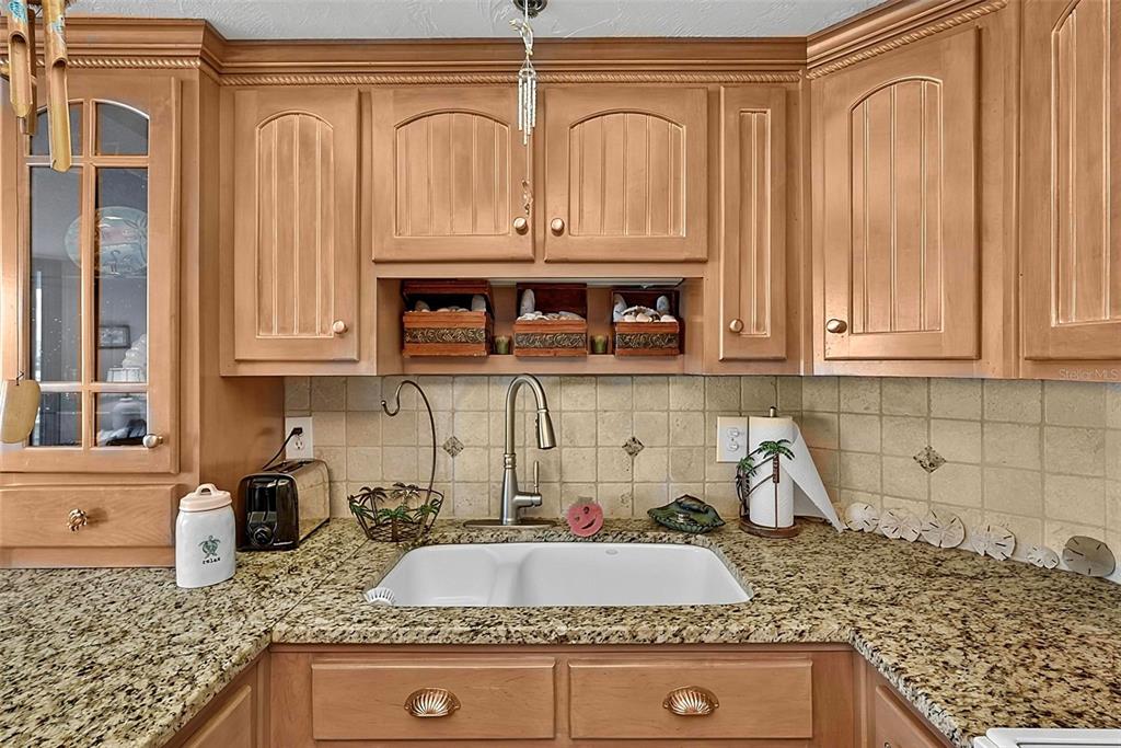 A kitchen sink area features light wood cabinets, granite countertops, and a tiled backsplash — 3013 S ATLANTIC AVENUE UNIT 2060, DAYTONA BEACH, FL