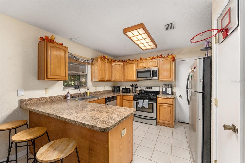 A kitchen with wood cabinets, laminate countertops, stainless steel appliances, and a breakfast bar — 3025 W UNIVERSITY AVENUE, GAINESVILLE, FL