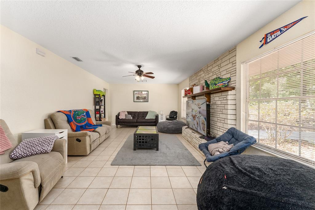 A living room features tile flooring, a stone fireplace, and a ceiling fan — 3025 W UNIVERSITY AVENUE, GAINESVILLE, FL